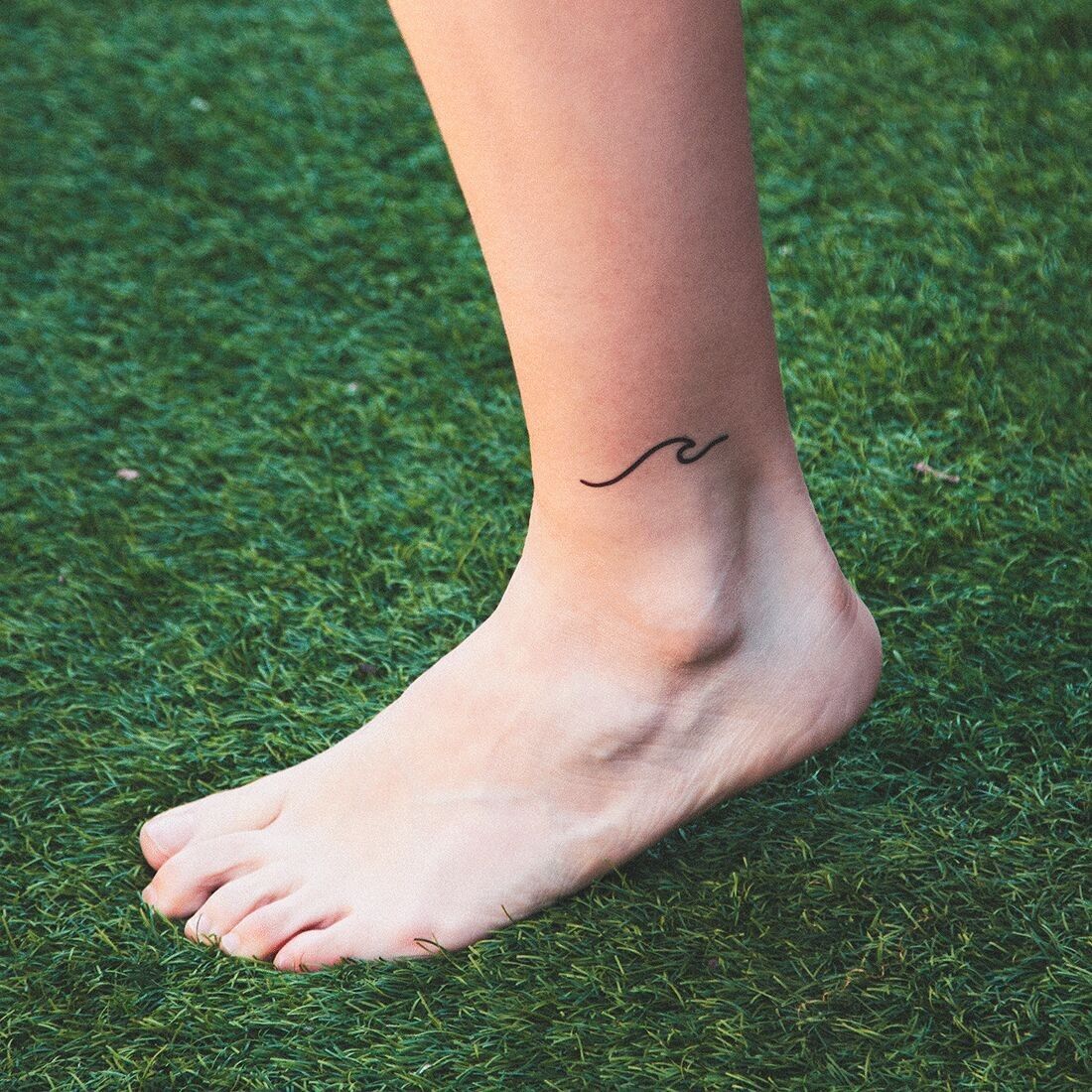 Minimalistic tiny wave tattoo placed on the achilles.